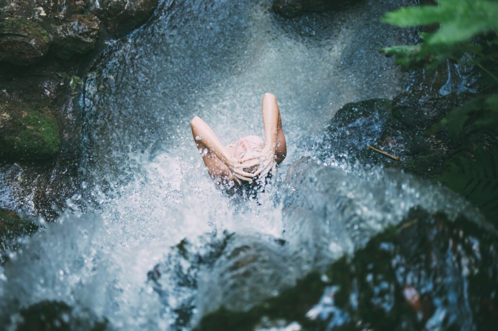 Žena se sprchuje pod vodopádem.