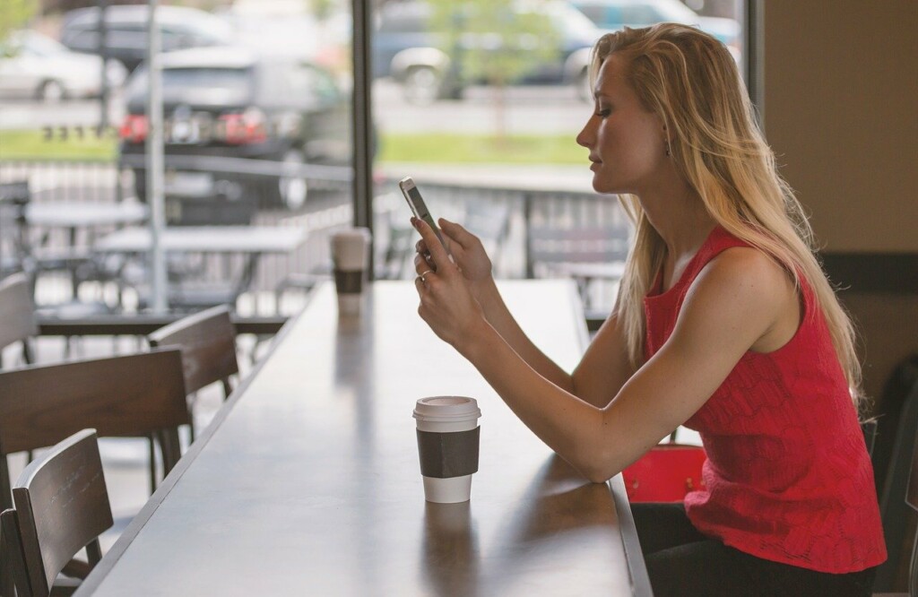 Dívka sedí v kavárně s telefonem.