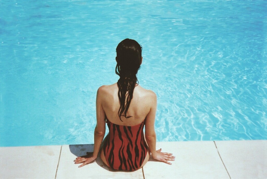 Žena v plavkách sedící u bazénu.