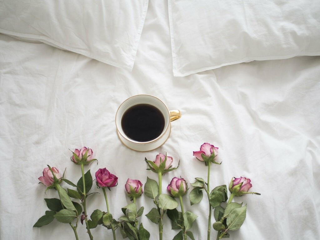 Šálek kávy na posteli s květinami.