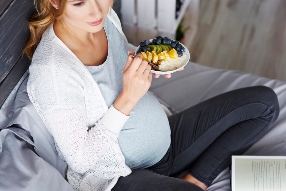 Těhotná žena s miskou jídla v ruce.