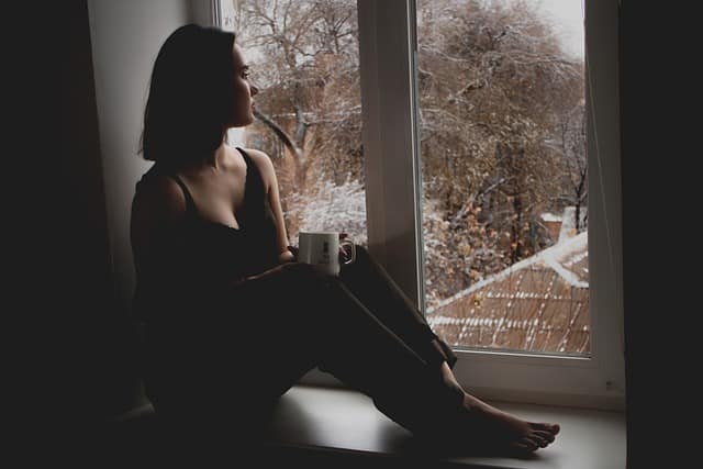 Žena sedící smutně u okna.