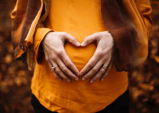 Těhotná žena s rukama ve tvaru srdce před bříškem.