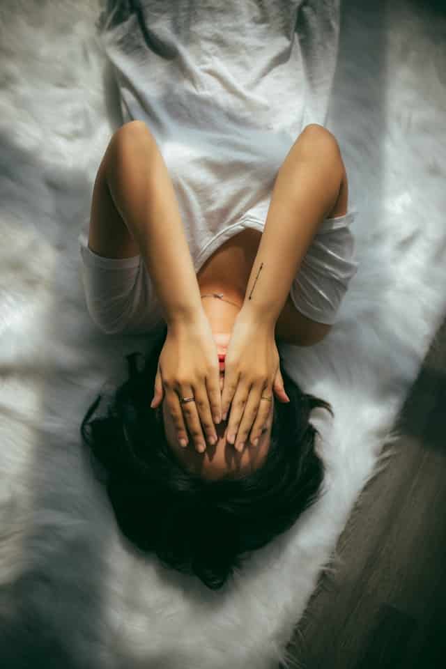 Žena si po probuzení zakrývá v posteli obličej rukama.