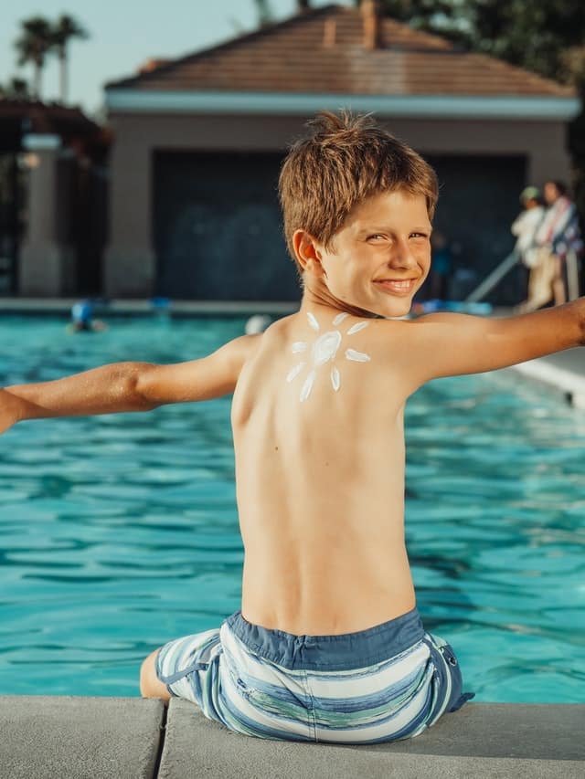 Chlapec u bazénu s opalovacím krémem na zádech.